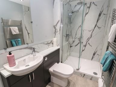 A bathroom with a sink, toilet, shower area with glass door, and towel rails at Pelham House in Keswick