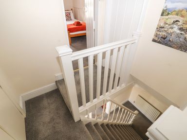 A carpeted staircase with white railing and a hallway leading to a bedroom with a bed and orange towels at Pelham House in Keswick