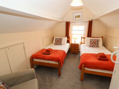 A bedroom with two single beds a wooden nightstand with a lamp and a checkered armchair at Pelham House in Keswick