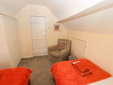A bedroom with two single beds with orange blankets and towels a checked armchair a white wardrobe and a white wooden door at Pelham House Keswick