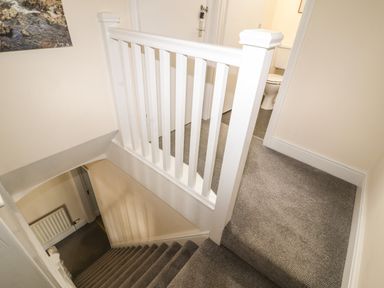 A stairway with a white banister leading down and a hallway with a bathroom at Pelham House in Keswick