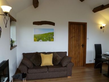 A living room with a brown sofa with cushions a wooden door a dining table with chairs and wall lights at Buttercup Cottage in Catterlen