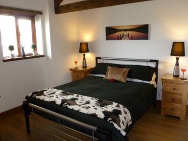 A bedroom with a double bed black bedding bedside tables with lamps and wine glasses at Buttercup Cottage in Catterlen