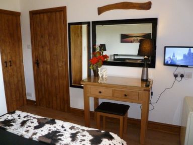 A bedroom with a wooden dressing table and stool next to a wall-mounted TV at Buttercup Cottage in Catterlen