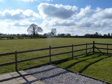 A fenced grassy field with trees in the distance under a cloudy sky at Buttercup Cottage in Catterlen