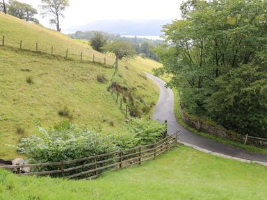 A winding road through a green rural landscape with wooden fences and trees at Low Skelgill in Troutbeck