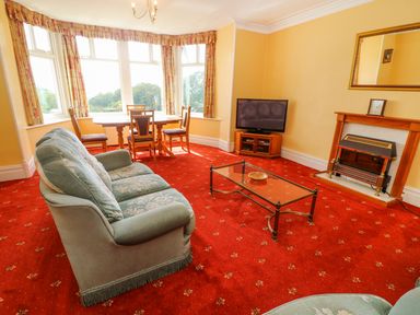 A living room with a sofa a glass coffee table a dining table with chairs a television and a fireplace at Low Skelgill in Troutbeck