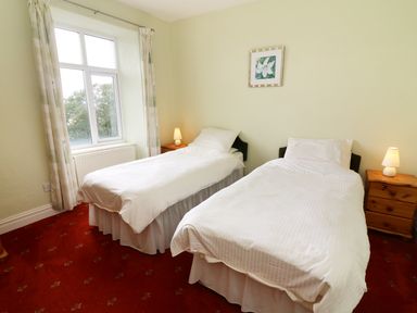 A bedroom with two single beds with white bedding bedside tables and lamps at Low Skelgill in Troutbeck