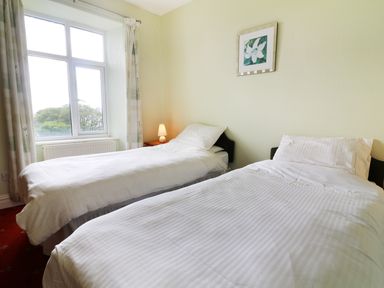A bedroom with two single beds white bedding a window with curtains and a bedside table lamp at Low Skelgill in Troutbeck