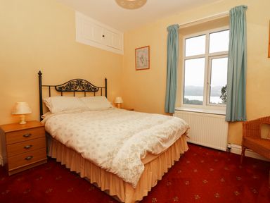 A bedroom with a double bed bedside tables lamps a window with curtains and a wicker chair at Low Skelgill in Troutbeck