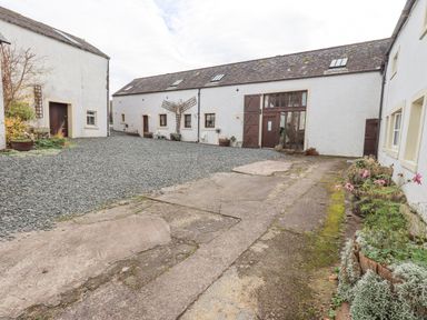 An outdoor courtyard with white buildings gravel ground and potted plants at Tithe Cottage in Cockermouth