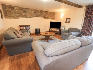 A living room with sofas a round wooden coffee table a television on a stand bookshelf and stone accent wall at Tithe Cottage in Cockermouth