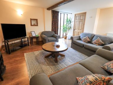 A living room with sofas a round coffee table a television and a plant at Tithe Cottage in Cockermouth