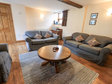 A living room with two grey sofas a wooden round coffee table and a rug at Tithe Cottage in Cockermouth