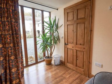A corner of a room with wooden door tall windows a potted plant and a waste bin at Tithe Cottage in Cockermouth