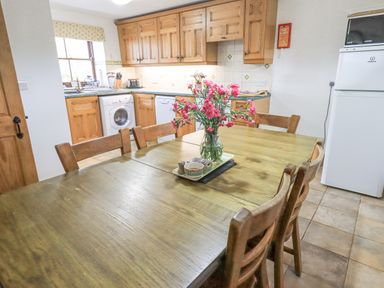 A kitchen with wooden cabinets a dining table with chairs and flowers in a vase at Tithe Cottage in Cockermouth