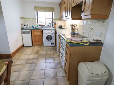 A kitchen with wooden cabinets appliances and a trash bin at Tithe Cottage in Cockermouth