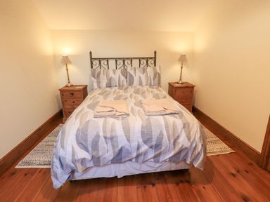 A bedroom with a double bed two bedside tables with lamps and folded towels on the bed at Tithe Cottage in Cockermouth