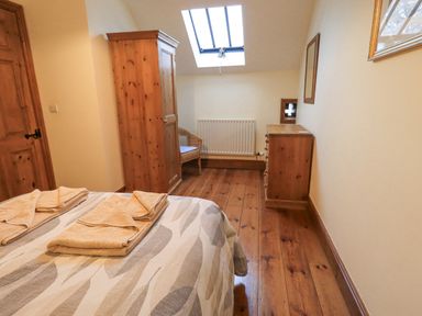 A bedroom with a bed, folded towels, wooden wardrobe, chest of drawers, chair, and skylight window at Tithe Cottage in Cockermouth
