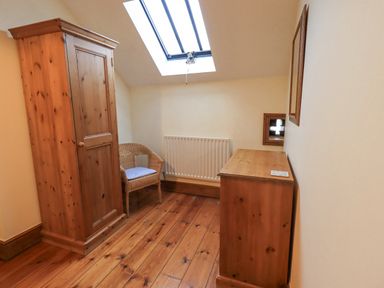 A small room with wooden wardrobe desk and chair under a skylight window at Tithe Cottage in Cockermouth