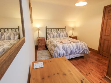 A bedroom with a double bed two bedside tables and lamps a wooden door and wooden floor at Tithe Cottage in Cockermouth