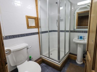 A bathroom with a toilet shower cubicle and pedestal sink at Tithe Cottage in Cockermouth