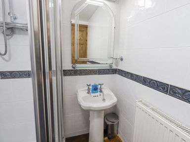 A bathroom sink with a mirror above and a shower visible to the left at Tithe Cottage in Cockermouth