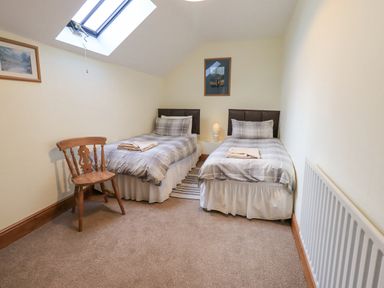 A bedroom with two single beds a wooden chair a small lamp and skylight window at Tithe Cottage in Cockermouth