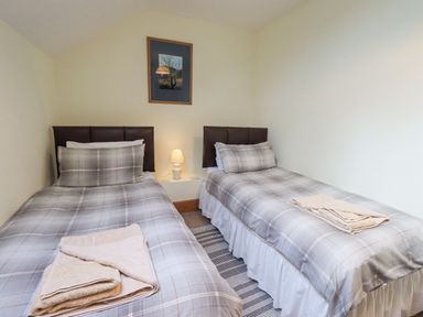 A bedroom with two single beds with gray plaid bedding a small lamp and a framed picture on the wall at Tithe Cottage in Cockermouth