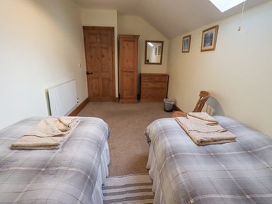 A bedroom with two single beds with folded towels on them a wooden door a wardrobe a dresser a mirror a chair and three pictures on the wall at Tithe Cottage in Cockermouth