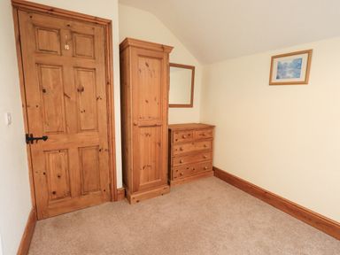A room with a wooden door, wooden wardrobe, wooden chest of drawers, mirror on wall, and framed picture at Tithe Cottage in Cockermouth