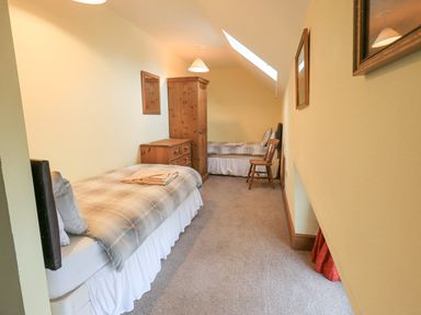 A bedroom with two single beds a wooden wardrobe a chest of drawers and a chair at Tithe Cottage in Cockermouth