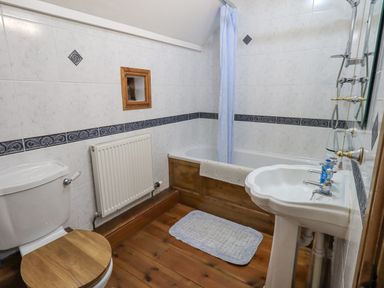 A bathroom with a toilet, sink, bathtub with a shower curtain and wooden flooring at Tithe Cottage in Cockermouth