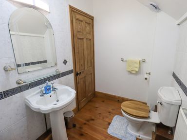 A bathroom with a pedestal sink and mirror a toilet with wooden seat and a wooden door at Tithe Cottage in Cockermouth