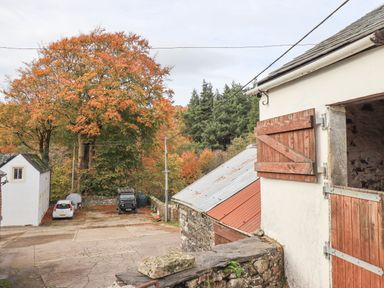An outdoor scene with buildings a parking area with two cars and trees with autumn leaves at Tithe Cottage in Cockermouth