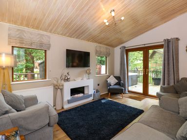 A living room with sofas a chair a black rug a wall-mounted television and glass doors at Footprints Lodge in Windermere
