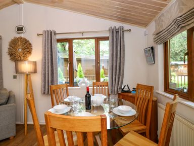 A dining area with a round glass table set with plates bowls wine glasses and a bottle of wine surrounded by wooden chairs at Footprints Lodge in Windermere