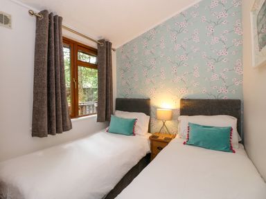 A bedroom with two single beds a nightstand with a lamp between them a window with curtains and floral wallpaper at Footprints Lodge in Windermere