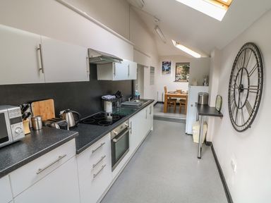 A kitchen with white cabinets black countertops and appliances with a dining area in the background at Long Crag Annexe in Ambleside
