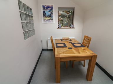 A small dining area with a wooden table and two chairs near a window with teapots and a welcome sign at Long Crag Annexe in Ambleside