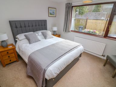 A bedroom with a double bed bedside tables lamps a window with curtains and a chair at Long Crag Annexe in Ambleside