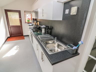 A kitchen with white cabinets black countertops a double sink and a wooden door at Long Crag Annexe in Ambleside