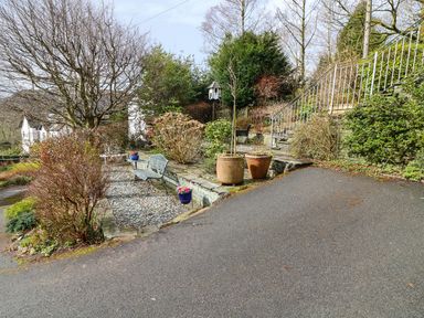 A garden area with benches stone steps potted plants and a birdhouse at Long Crag Annexe in Ambleside