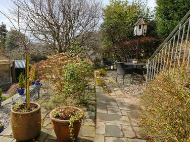 An outdoor patio area with potted plants stone pathway table and chairs and a birdhouse at Long Crag Annexe Ambleside
