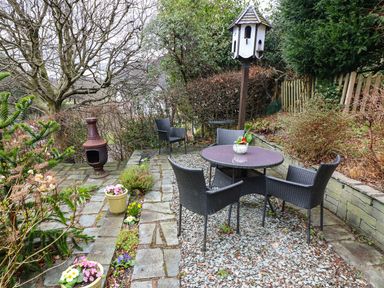 A patio area with a round table surrounded by black chairs and a birdhouse on a pole in a garden at Long Crag Annexe in Ambleside