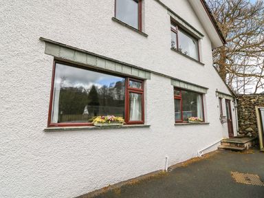 Exterior view of a white house with brown framed windows and flower boxes under two windows at Long Crag Annexe in Ambleside