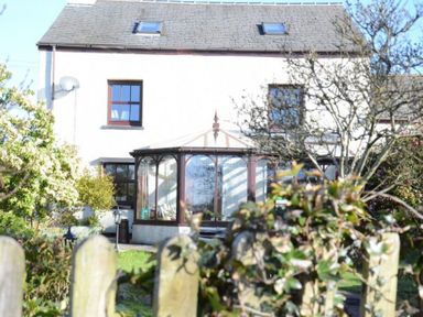 A house with a glass conservatory and garden behind a wooden fence at Greety Gate House in Foxfield