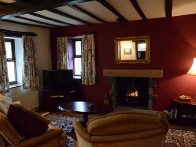 A living room with a fireplace a television floral curtains and wooden beams at Greety Gate House in Foxfield