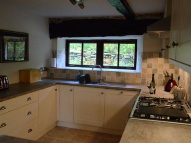 A kitchen with white cabinets a gas stove a window above the sink and various kitchen appliances at Greety Gate House in Foxfield