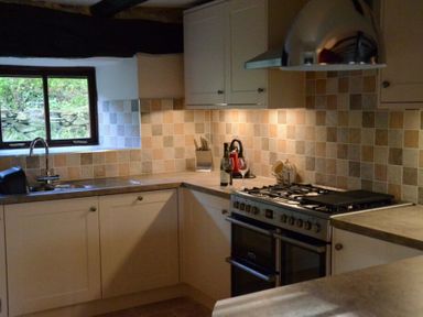 A kitchen with a sink under a window a countertop stove and beige tiled backsplash at Greety Gate House in Foxfield